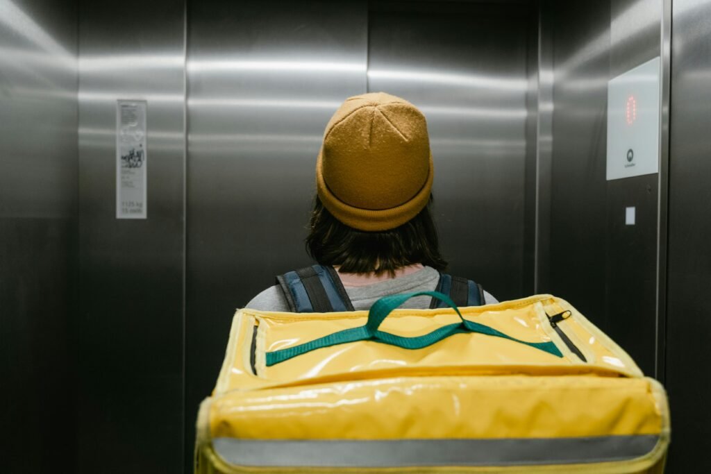 pexels photo 7706557 7706557 Back view of a delivery person with a yellow thermal bag inside an elevator.