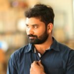 Home A thoughtful man with a beard and blue shirt posing indoors, displaying a stylish watch.
